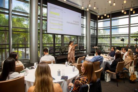 Plano aberto com a palestrante ao fundo e participantes sentados à mesa, voltados para o palco. (Grand Hyatt SP, Evento Corporativo, Fotos Bruno Arita)'