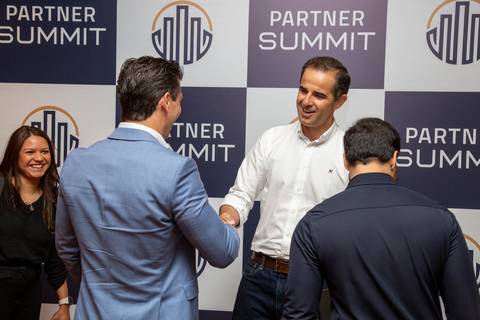 Participante cumprimentando outro convidado em frente ao backdrop do Partner Summit, no credenciamento. (Grand Hyatt SP, Evento Corporativo, Fotos Bruno Arita)'