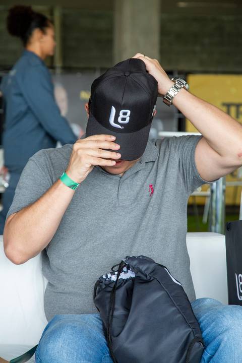 Participante sorridente colocando o boné de brinde com o logo da L8 Group e Ruckus Networks. (Stock Car 2025, Interlagos, Fotos Bruno Arita)'