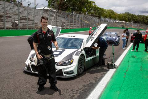 Participante da Ruckus Networks posando para foto em frente ao carro de corrida da Stock Car. (L8 Group, Ruckus Networks, Fotos Bruno Arita)'