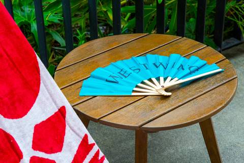 Leque personalizado da Westwing aberto sobre mesa de apoio na área da piscina. (Lançamento Verão 2026, São Paulo, Fotos Bruno Arita)'