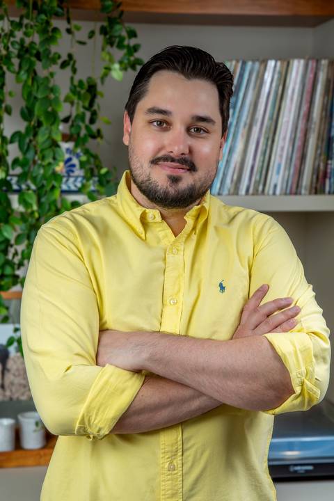 Retrato vertical de Tainan Salvador de braços cruzados, vestindo camisa amarela, transmitindo confiança e modernidade para perfil profissional. (LinkedIn, Fotos Bruno Arita)'