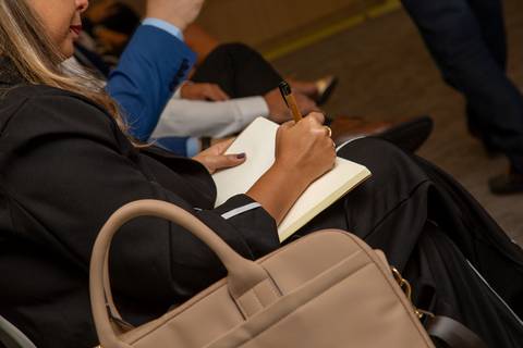 Plano detalhe das mãos de um participante anotando pontos da apresentação em caderno personalizado. (Treinamento Corporativo, Fotos Bruno Arita)'