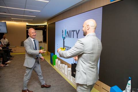 Wilson Arita recebendo premiação de Alex Karam com o logotipo da Unity em destaque no telão ao fundo. (MetLife SP, Fotos Bruno Arita)'