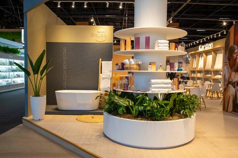 Estrutura de entrada do estande com itens de perfumaria em prateleiras circulares e banheira decorativa ao fundo. (ABUP Show 2026, Fotos Bruno Arita)'