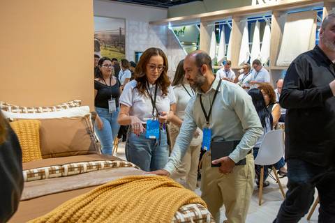 Vendedora e cliente sentindo o tecido de coberta marrom em cama de exposição. (ABUP Show 2026, Fotos Bruno Arita)'
