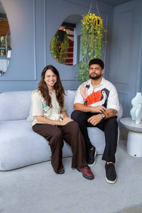 Clara Nahas e João Gabriel, embaixadores Westwing 2026, sentados em sofá orgânico cinza na loja da Vila Madalena em foto vertical. Fotografia editorial de marca por Bruno Arita.'