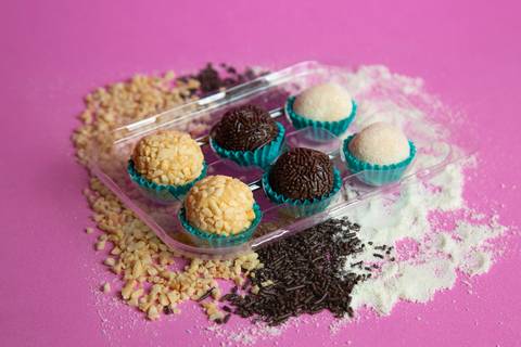 Caixa com 6 brigadeiros sortidos (amendoim, tradicional e ninho) disposta sobre elementos que compõem o sabor. Foto por Bruno Arita.'