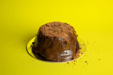 Foto de um Mini Bolo Vulcão de Ovomaltine da Bem Caseirinho SP, Morumbi, com cobertura cremosa transbordando. A imagem foca na textura e no apelo visual caseiro para e-commerce e iFood.'