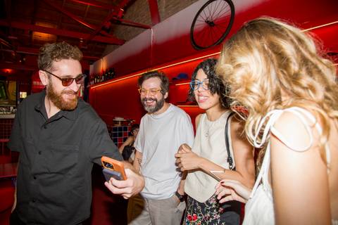 Erika e amigos rindo ao ver celular em momento descontraído de aniversário. Fotografia: Bruno Arita.'