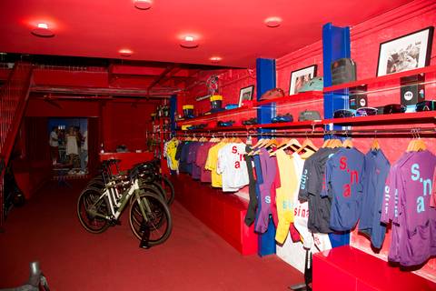 Interior da loja Sina Café com uniformes de ciclismo e produtos expostos para atendimento. Registro por Bruno Arita.'