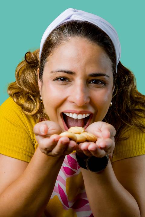 Close-up de Renata Mendes insinuando comer biscoitos artesanais nas suas mãos, transmitindo acolhimento e sabor caseiro. Fotografia: Bruno Arita.'