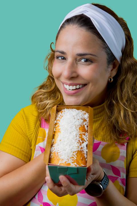 Plano detalhe de Renata Mendes segurando o bolo de coco gourmet, focando na textura e qualidade do doce. Foto por Bruno Arita.'