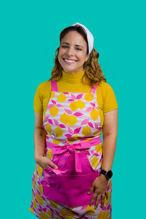 Retrato de posicionamento de Renata Mendes com sorriso acolhedor e avental de limões em fundo turquesa. Foto por Bruno Arita.'