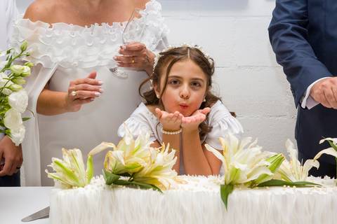 Filha do casal posando de forma divertida e alegre em frente à mesa do bolo de casamento. Foto por Bruno Arita.'