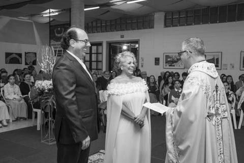 Noivo Danilo e noiva Tabatha rindo de forma leve e espontânea em frente ao padre. Fotografia PB por Bruno Arita no Morumbi.'