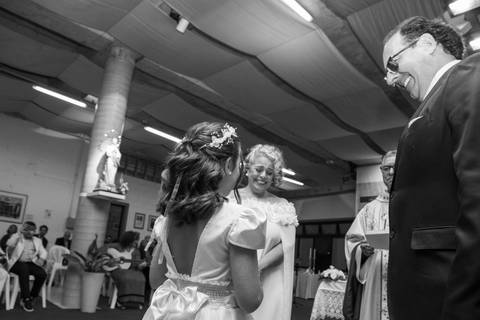 Perspectiva em contra-plongé da filha chegando com as alianças e os pais sorrindo. Fotografia espontânea em PB por Bruno Arita.'
