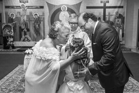 Noiva Tabatha beija a filha e o pai sorri ao receberem as alianças com o padre ao fundo. Foto PB por Bruno Arita.'