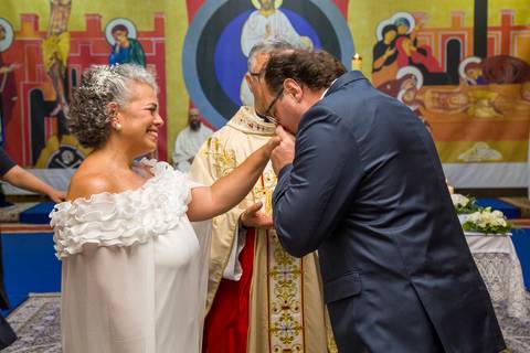Fotografia colorida do noivo Danilo beijando a aliança já colocada na mão da noiva Tabatha. Foto por Bruno Arita.'