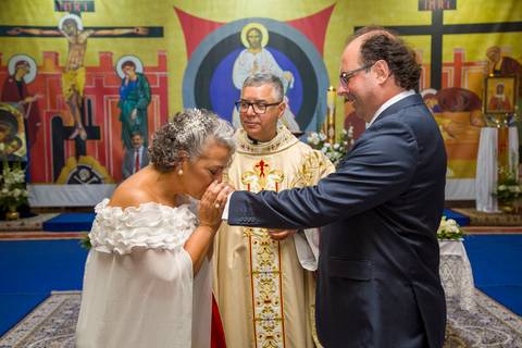Fotografia colorida da noiva Tabatha beijando a aliança já colocada na mão do noivo Danilo. Registro por Bruno Arita.'
