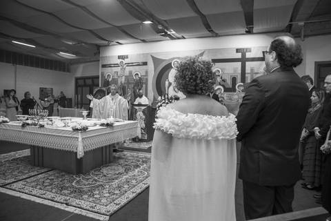 Noivos em primeiro plano de costas com vista do padre celebrando no altar ao fundo. Foto por Bruno Arita.'