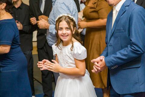 Filha do casal sorrindo e olhando para a câmera durante a tradicional dança ao redor da mesa. Foto por Bruno Arita.'