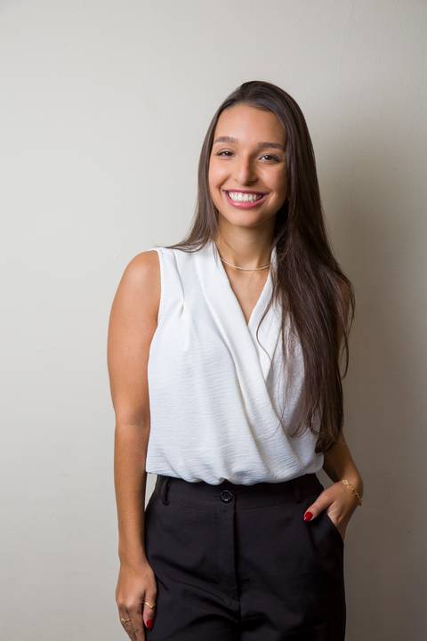 Foto profissional de jovem médica sorrindo com a mão no bolso, usando blusa transpassada branca e calça preta por Bruno Arita. Fotografia corporativa realizada para a SCOPO MetLife no Centro de Convenções Rebouças.'