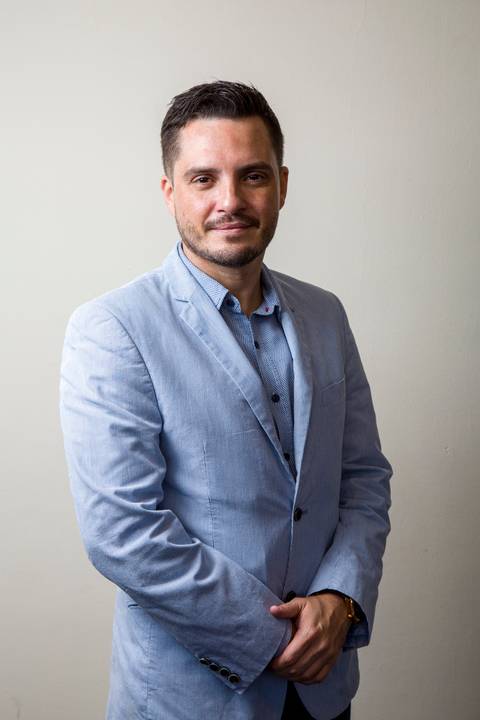 Fotografia de perfil profissional de médico com as mãos cruzadas, vestindo blazer cinza claro e camisa azul por Bruno Arita. Imagem de liderança para a ação da SCOPO MetLife no Centro de Convenções Rebouças em SP.'