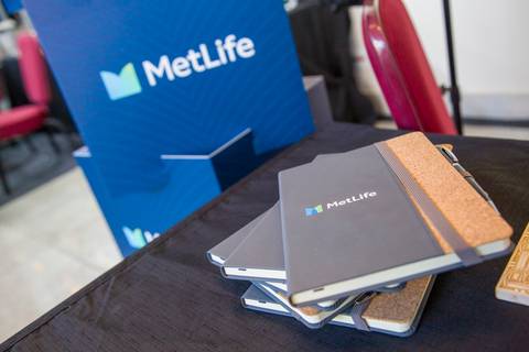 Close em cadernos de brinde com capa cinza, detalhes em cortiça e logo da MetLife sobre mesa preta. Fotografia de detalhes por Bruno Arita no Centro de Convenções Rebouças.'
