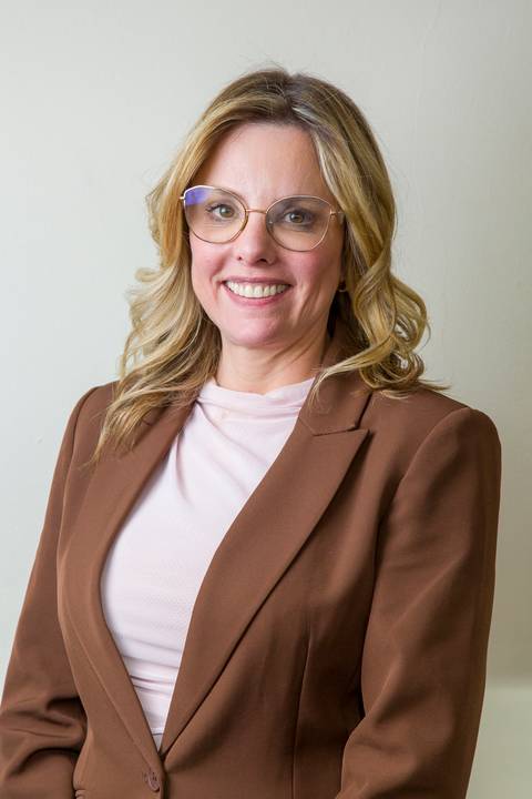 Close de retrato de médica sorridente com óculos de grau, blazer marrom e blusa rosa clara, por Bruno Arita. Foto corporativa focada em credibilidade para a SCOPO MetLife no Centro de Convenções Rebouças.'