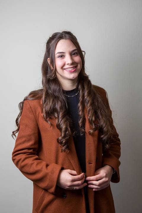Foto de perfil de médica sorridente com cabelos longos ondulados, usando casaco marrom terracota e blusa preta, por Bruno Arita. Registro para LinkedIn na ativação da SCOPO MetLife no Centro de Convenções Rebouças.'