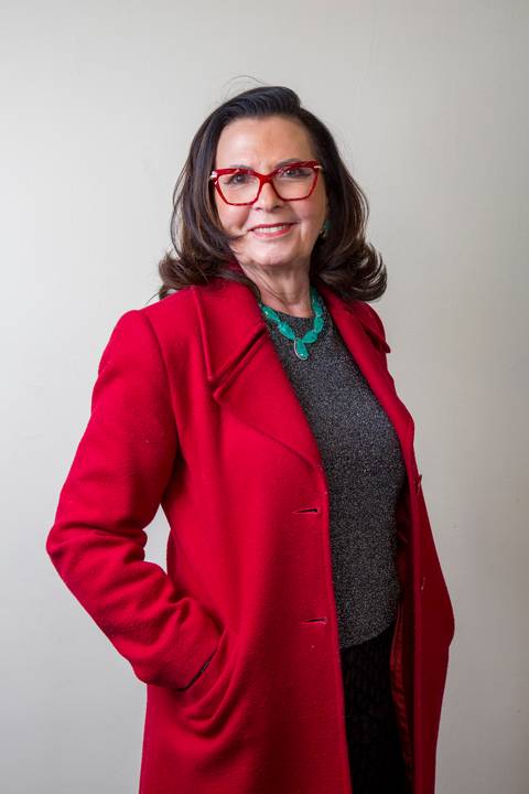 Médica sênior de óculos vermelhos, sobretudo vermelho vibrante e colar verde com a mão no bolso. Retrato corporativo de autoridade por Bruno Arita para SCOPO MetLife no Centro de Convenções Rebouças.'