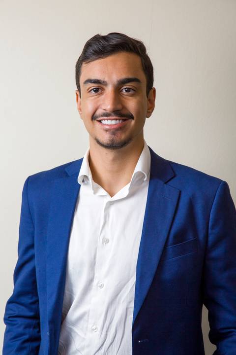 Jovem médico sorridente com blazer azul bic e camisa branca de botão aberta no colarinho. Retrato de posicionamento profissional por Bruno Arita na ação da SCOPO MetLife no Centro de Convenções Rebouças.'