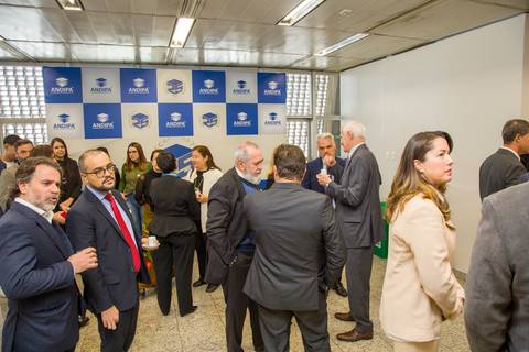 Visão geral da recepção movimentada no foyer da FIESP com painel de fundo dos 25 anos da ANDIPA. Foto de cobertura por Bruno Arita.'