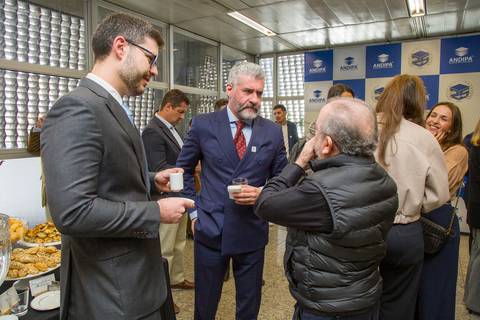 Convidados alinhados conversando com xícaras de café no foyer da FIESP durante o evento da ANDIPA com painel de 25 anos ao fundo. Registro espontâneo por Bruno Arita.'