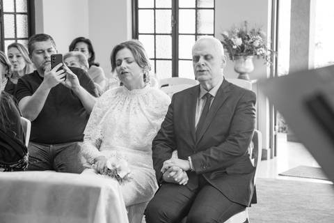 Noivos Ana Paula e Antonio Carlos sentados no altar durante a celebração religiosa. Fotografia em P&B por Bruno Arita.'