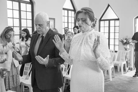 Noivos e convidados de mãos erguidas em momento de oração e fé na Capela Santa Suzana. Foto por Bruno Arita.'