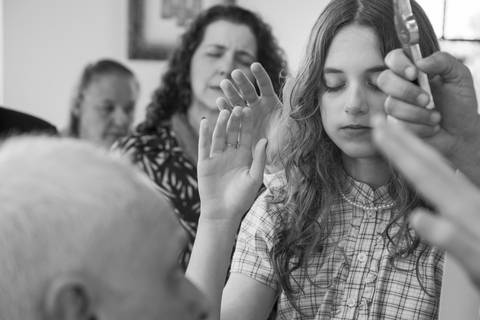 Padre e noivos impondo as mãos sobre a cabeça da filha em oração de bênção familiar. Foto por Bruno Arita.'