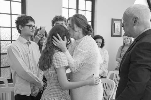 Noiva abraçando e beijando a cabeça da filha em gesto carinhoso na capela. Foto em família por Bruno Arita.'
