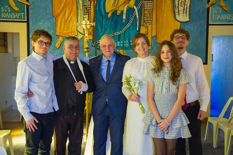 Foto oficial dos noivos com os filhos e o padre celebrante no painel da igreja. Foto por Bruno Arita.'