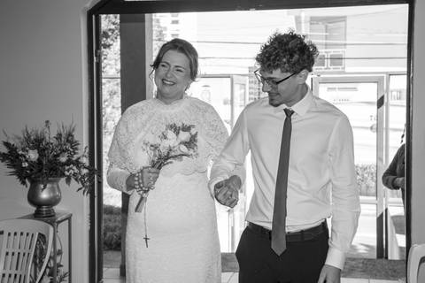 Noiva Ana Paula sorrindo ao entrar na igreja de braço dado com seu filho. Fotografia de casamento por Bruno Arita.'