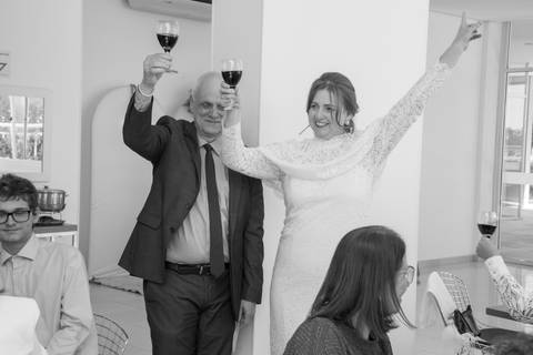 Noivos de braços erguidos com taças de vinho comemorando com muita alegria. Foto por Bruno Arita.'