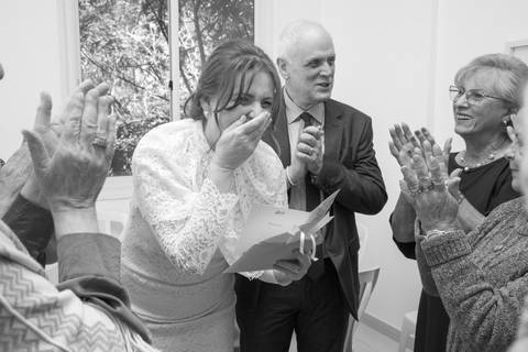 Noiva sorrindo e levando a mão ao rosto emocionada durante as homenagens no salão. Foto por Bruno Arita.'