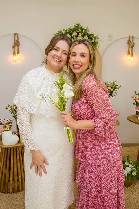 Noiva Ana Paula sorrindo ao lado da amiga que pegou o buquê de flores brancas. Foto por Bruno Arita.'
