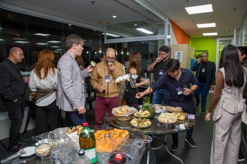 Convidados reunidos ao redor da mesa de buffet aproveitando o momento de networking. Foto por Bruno Arita.'