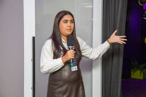 Apresentadora com microfone na mão discursando para os convidados na inauguração do estúdio. Foto por Bruno Arita.'