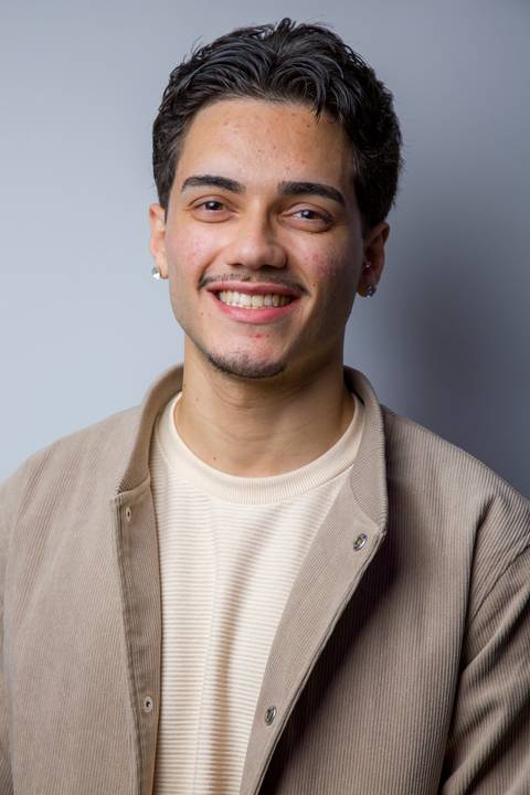 Retrato de jovem sorridente vestindo jaqueta bege em sessão de fotos de perfil profissional. Foto por Bruno Arita.'