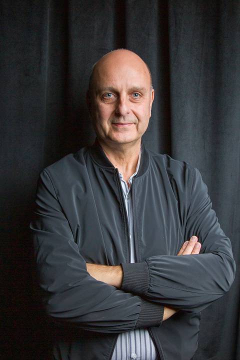 Retrato corporativo profissional de homem de jaqueta preta de braços cruzados sobre fundo escuro. Foto por Bruno Arita.'
