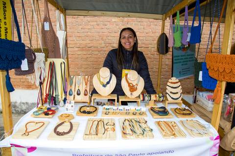 Empreendedora posando em barraca de bijuterias e colares artesanais feitos à mão. Foto por Bruno Arita.'