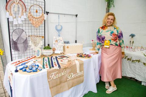 Empreendedora sorridente posando em sua barraca de artesanato em macramê e decorações. Foto por Bruno Arita.'